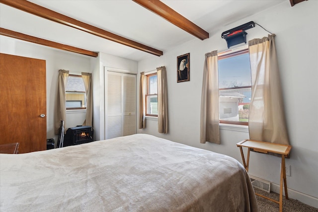 701 N Saginaw St, Durand, MI 48429 - carpeted bedroom with beamed ceiling, multiple windows, a wood stove, and a closet