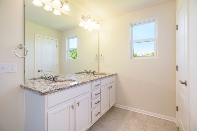 bathroom with baseboards, tile patterned floors, double vanity, and a sink