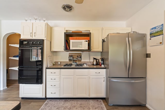 2250 Saines Manor Dr, Jackson, MI 49201 - kitchen featuring gas stovetop, dobule oven black, arched walkways, freestanding refrigerator, and wood finished floors