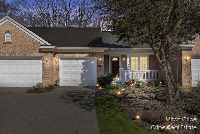 townhome / multi-family property with covered porch, brick siding, a shingled roof, and driveway