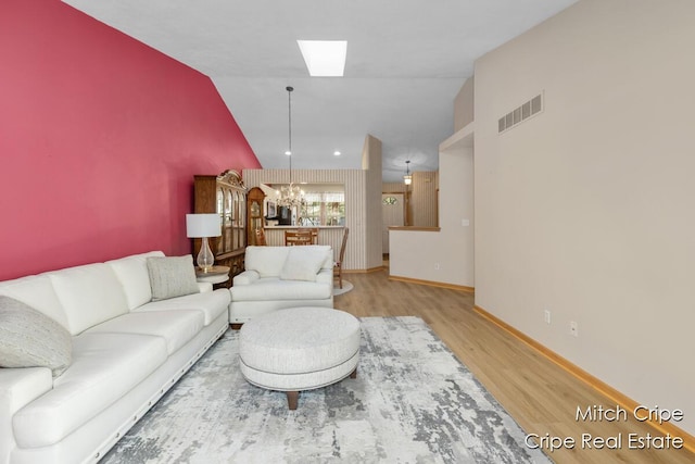 living area featuring a notable chandelier, visible vents, vaulted ceiling, baseboards, and wood finished floors