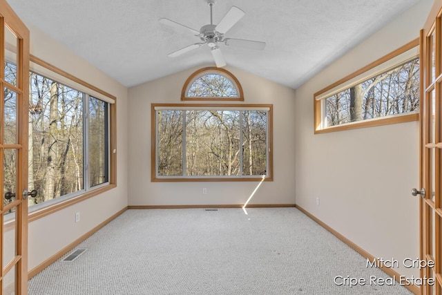 carpeted empty room with lofted ceiling, visible vents, plenty of natural light, and baseboards