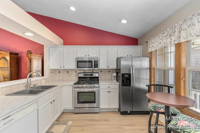 kitchen featuring lofted ceiling, white cabinetry, a sink, appliances with stainless steel finishes, and light countertops