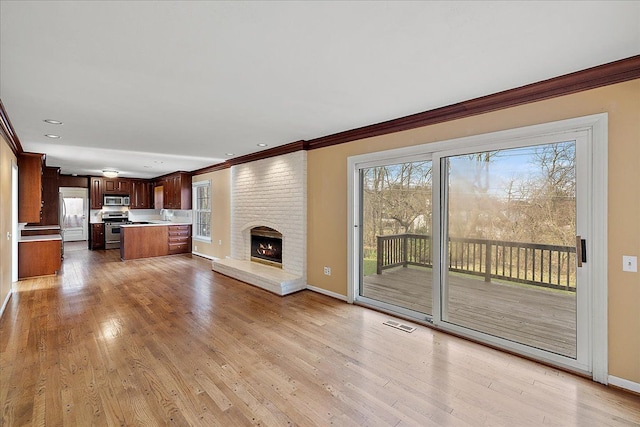 unfurnished living room with baseboards, ornamental molding, a wealth of natural light, and a brick fireplace