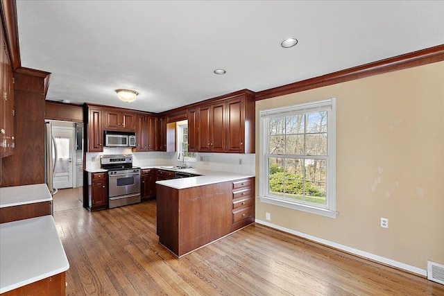 kitchen with a sink, stainless steel appliances, light countertops, wood finished floors, and a peninsula