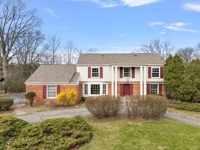 view of front of property with driveway, roof with shingles, a front lawn, and brick siding