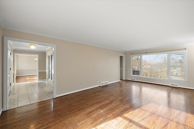 empty room with baseboards, visible vents, wood finished floors, and crown molding