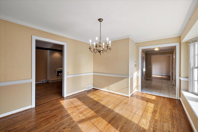 unfurnished room featuring visible vents, wood finished floors, a notable chandelier, and a lit fireplace