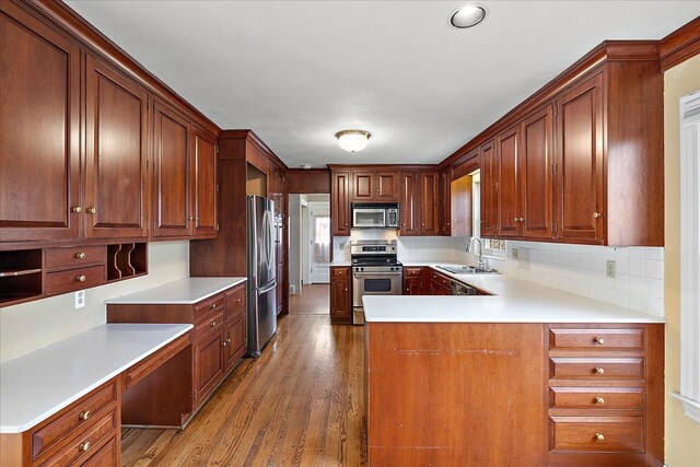 kitchen with tasteful backsplash, a sink, appliances with stainless steel finishes, wood finished floors, and a peninsula