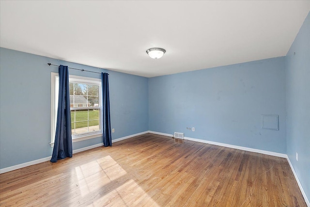 empty room with wood finished floors, visible vents, and baseboards