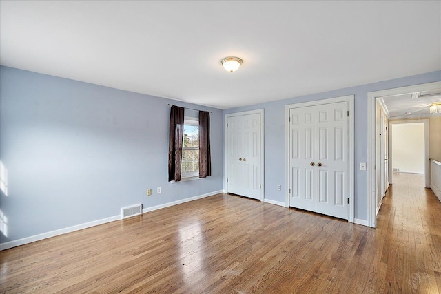unfurnished bedroom with baseboards, visible vents, wood finished floors, and multiple closets