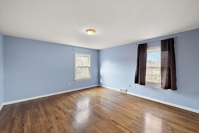 unfurnished room with a wealth of natural light, visible vents, wood finished floors, and baseboards