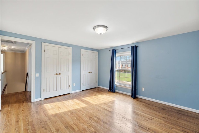 unfurnished bedroom featuring baseboards, multiple closets, and light wood-style floors