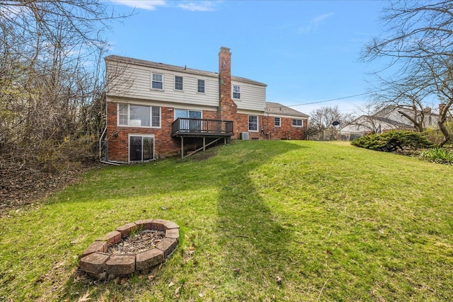 rear view of house with a chimney, a lawn, brick siding, a deck, and a fire pit