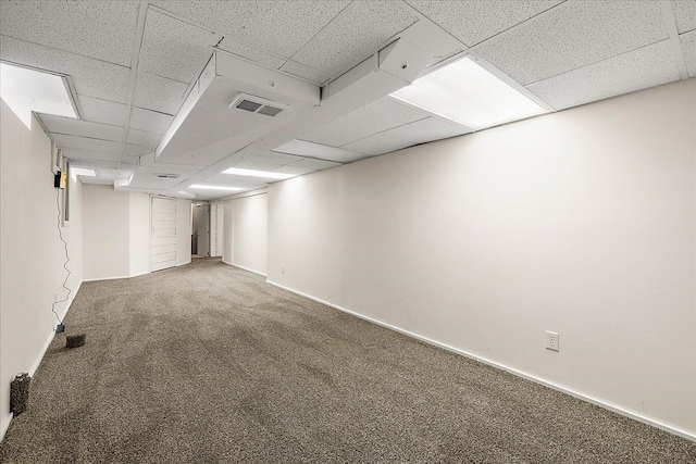 finished below grade area with a paneled ceiling, carpet flooring, baseboards, and visible vents