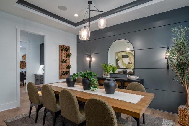 dining area featuring a tray ceiling, light wood finished floors, and baseboards