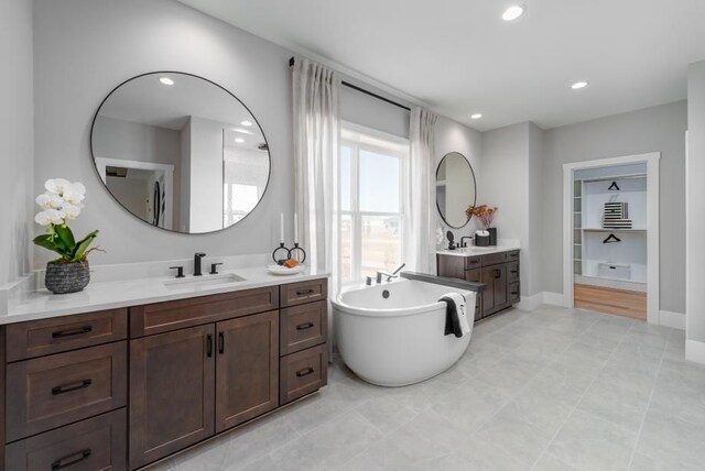 bathroom with a soaking tub, recessed lighting, two vanities, and a sink
