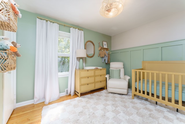 bedroom with a nursery area, wood finished floors, and a decorative wall