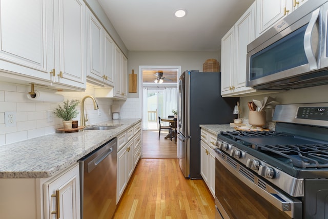 kitchen featuring backsplash, appliances with stainless steel finishes, a sink, white cabinets, and light wood-style floors