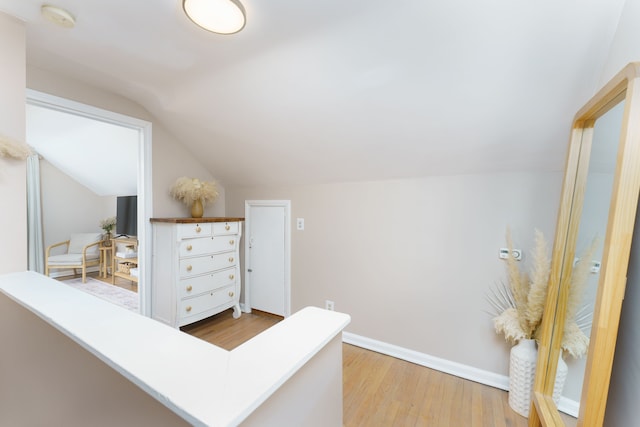 hall featuring light wood-style floors, baseboards, and vaulted ceiling