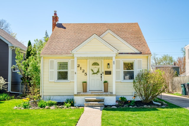 bungalow-style house featuring a shingled roof, fence, a front yard, and a chimney