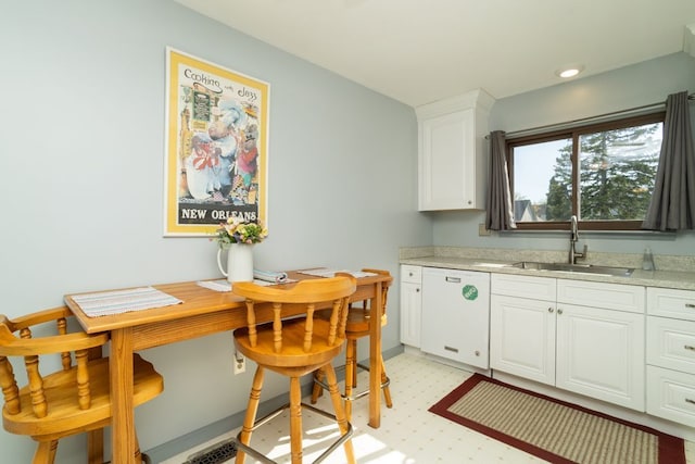 kitchen with light floors, white dishwasher, white cabinets, a sink, and baseboards