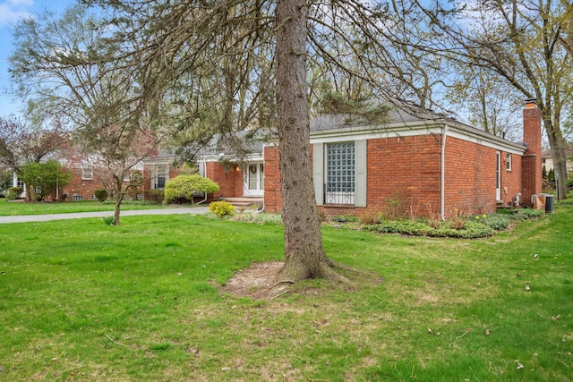 view of front facade with brick siding, a front yard, and a chimney