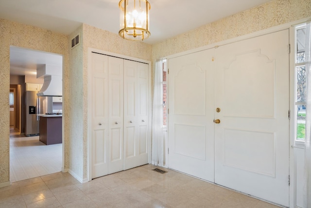 tiled foyer entrance featuring a notable chandelier, visible vents, and wallpapered walls