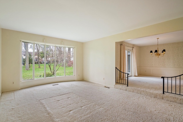 carpeted spare room featuring visible vents, a chandelier, and baseboards