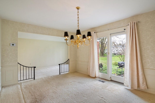 carpeted empty room featuring a chandelier, a wainscoted wall, visible vents, a decorative wall, and wallpapered walls