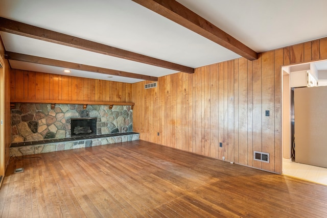 unfurnished living room featuring beamed ceiling, visible vents, wood walls, and hardwood / wood-style flooring