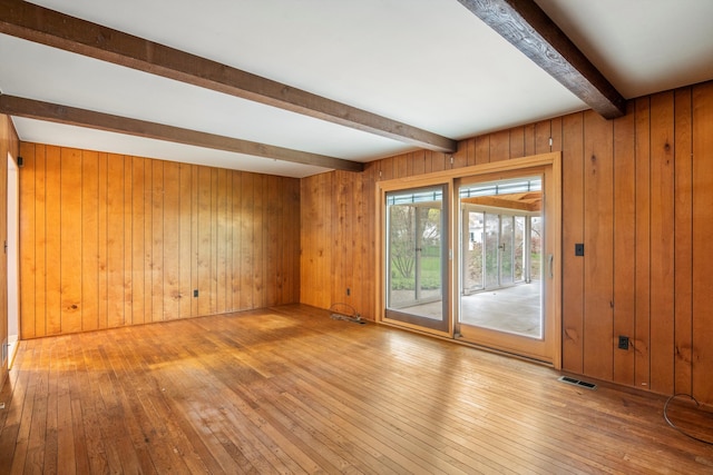 spare room featuring beamed ceiling, wooden walls, visible vents, and hardwood / wood-style flooring