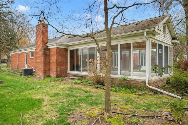 rear view of house featuring cooling unit, a chimney, a lawn, brick siding, and a sunroom