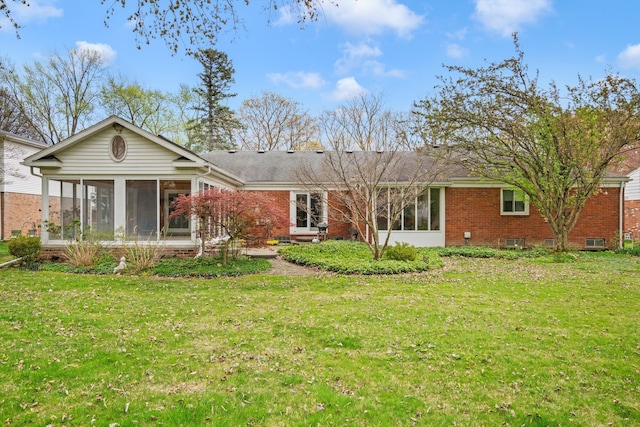 back of property featuring a sunroom, a yard, and brick siding