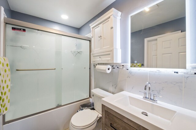 bathroom with backsplash, tile walls, vanity, combined bath / shower with glass door, and toilet