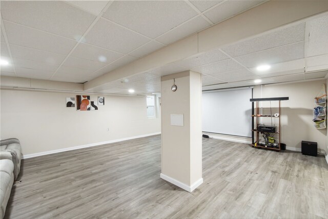 finished below grade area with baseboards, a drop ceiling, and wood finished floors
