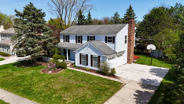 traditional home featuring an attached garage, a front lawn, a porch, a chimney, and driveway