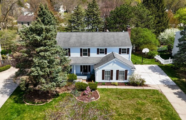 view of front of house with fence, a front yard, roof with shingles, a chimney, and driveway