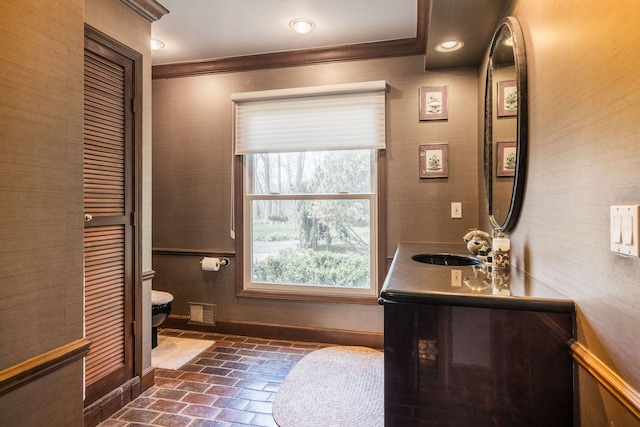 bathroom with crown molding, baseboards, vanity, toilet, and brick floor