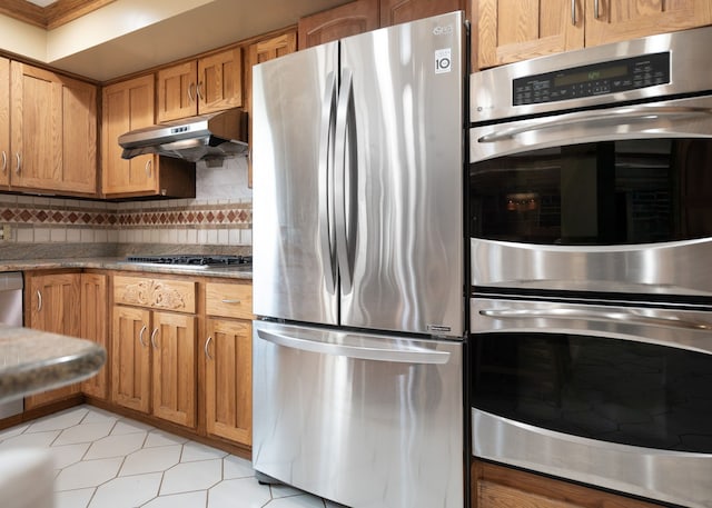kitchen featuring under cabinet range hood, brown cabinets, appliances with stainless steel finishes, and tasteful backsplash