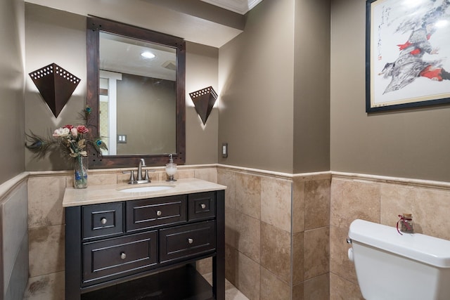 half bath featuring vanity, toilet, tile walls, and a wainscoted wall