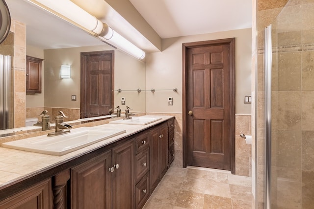 full bathroom with a sink, a wainscoted wall, a tile shower, and tile walls