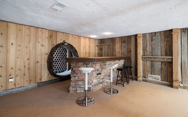 bar with visible vents, carpet flooring, wooden walls, a textured ceiling, and a dry bar