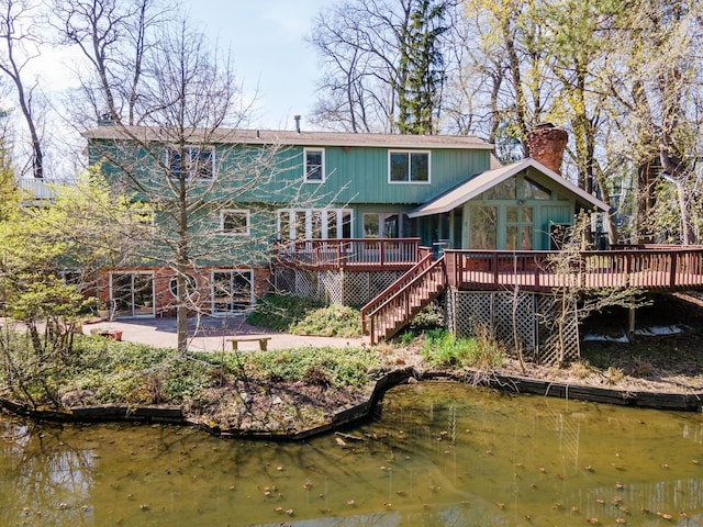 rear view of house with stairway, a patio, a chimney, and a deck with water view
