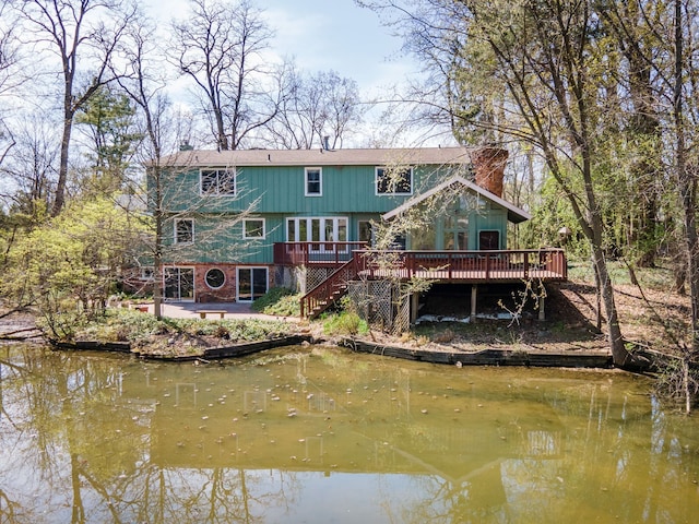 rear view of house with stairs, a patio area, a deck with water view, and a chimney