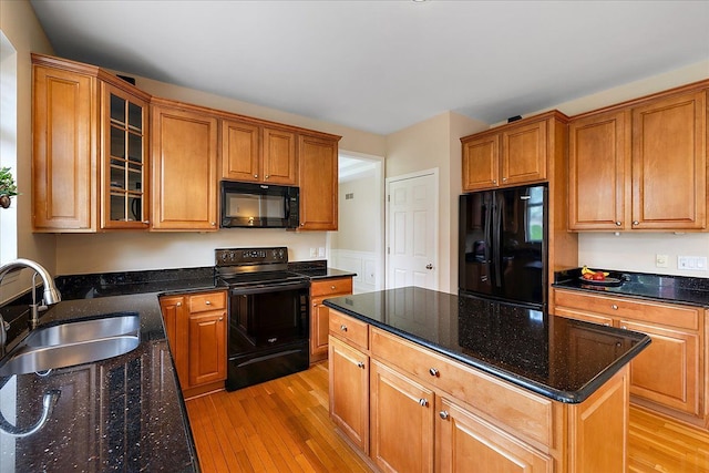 kitchen with a kitchen island, a sink, black appliances, glass insert cabinets, and light wood-style flooring