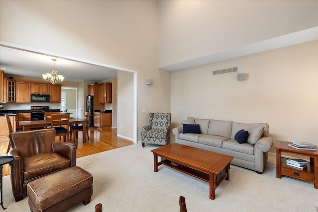 living area with visible vents, baseboards, a chandelier, a high ceiling, and light carpet