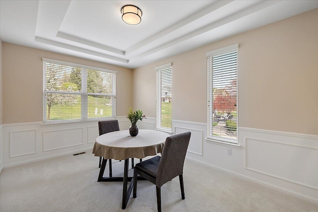 dining space with a raised ceiling, light carpet, a wainscoted wall, and visible vents