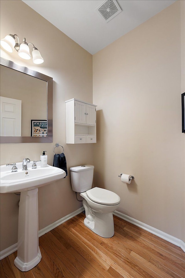 half bathroom featuring visible vents, wood finished floors, a sink, baseboards, and toilet