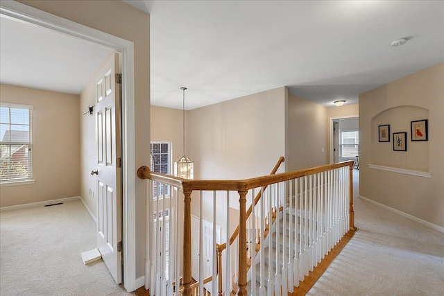 hall featuring a wealth of natural light, light colored carpet, and an upstairs landing